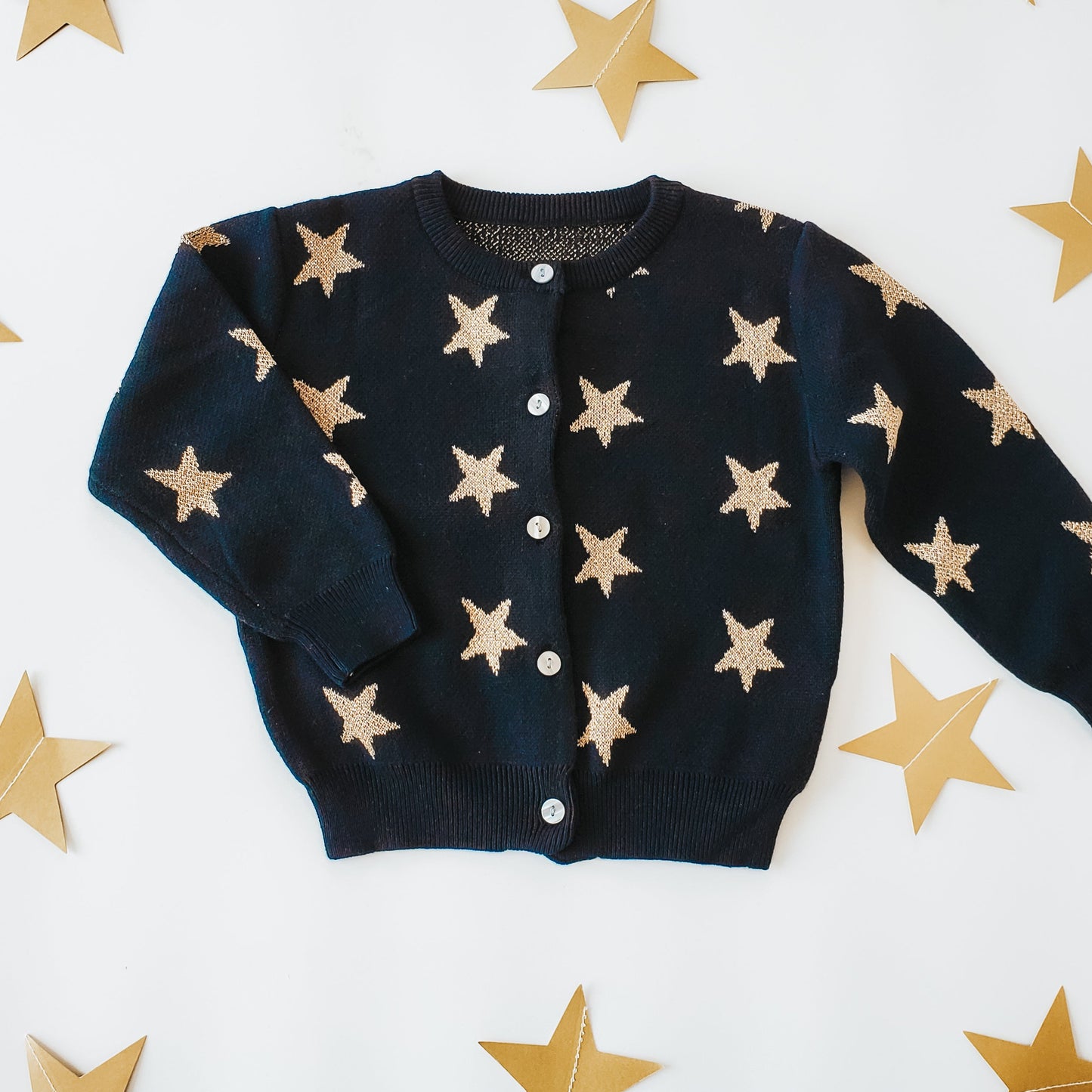 Black cardigan with beige star patterns on a white background with gold stars.