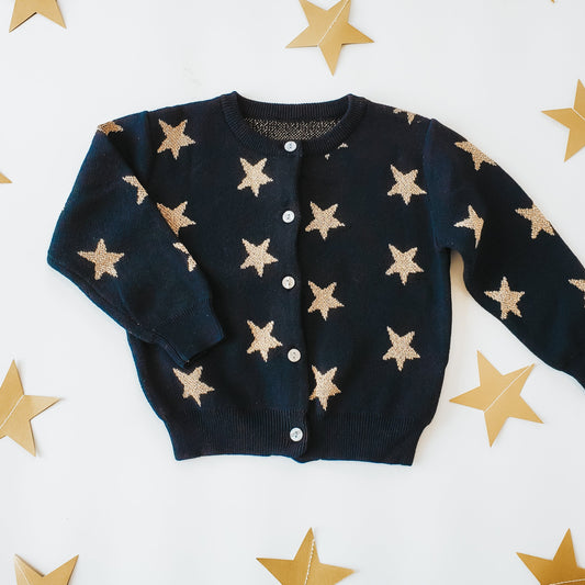 Black cardigan with beige star patterns on a white background with gold stars.