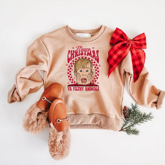 Beige sweatshirt with graphic design and red bow, paired with brown shoes and pine branches on a white background