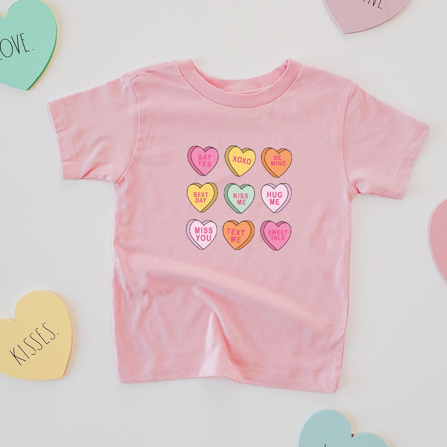 Pink baby romper with colorful heart designs surrounded by heart-shaped cards on a light gray background