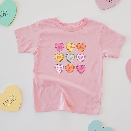 Pink baby romper with colorful heart designs surrounded by heart-shaped cards on a light gray background