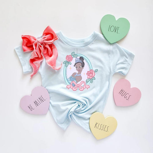 Light blue Darling Tiana T-shirt with a pink bow and roses design, surrounded by heart-shaped candies.