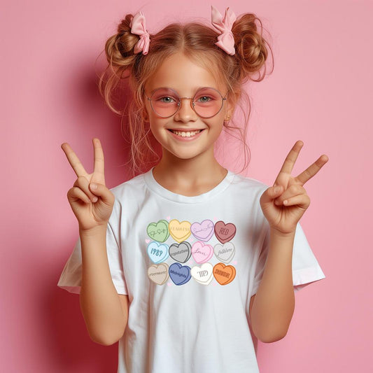 Smiling girl in a white Eras Valentine T-shirt with colorful heart-shaped album titles, pink bows, and sunglasses.