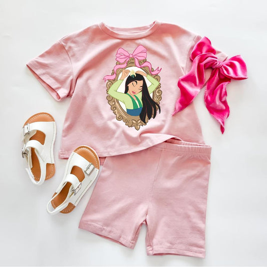 Pink cotton Fearless Warrior Biker Set with Mulan graphic tee and matching shorts, paired with white sandals and a pink bow.