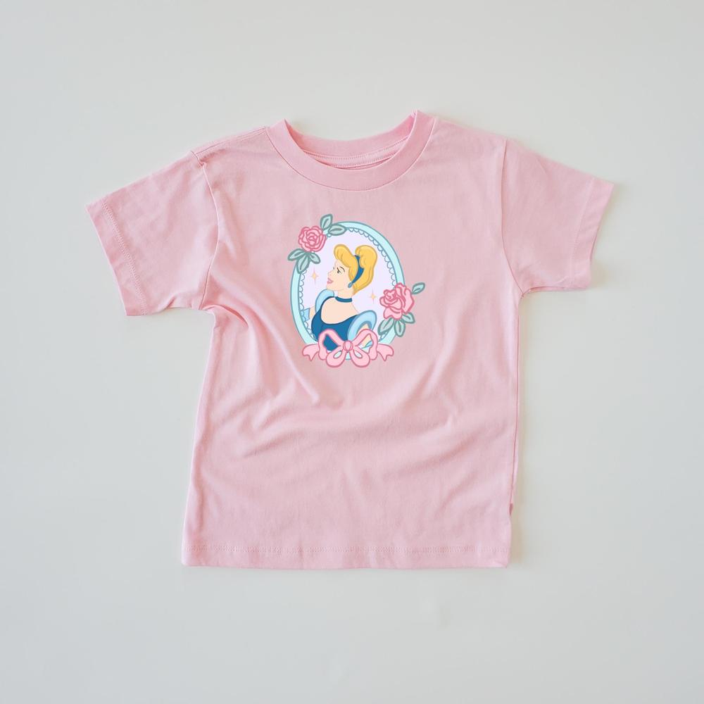 Pink short-sleeve t-shirt with a graphic of Cinderella in a blue dress, framed by pink roses and a bow.