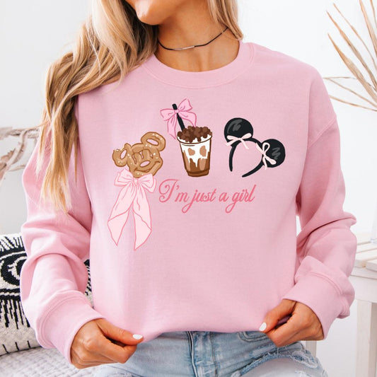 Pink crewneck sweater with "I'm just a girl" text, a The pretzel, drink, and The ears design.