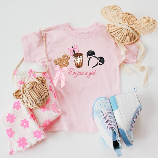 Pink "I'm Just a Girl" t-shirt with The Park-inspired treats, paired with floral pants, straw bag, and blue sneakers.