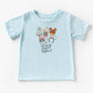 Light blue cotton kids t-shirt with "Infinity Snacks and Beyond" text and cartoon snacks like a rocket, drink, waffle, cupcake, and The ears.