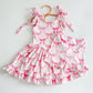 Pink activewear dress and biker shorts set with a playful bow print, ruffled hem, and shoulder ties.