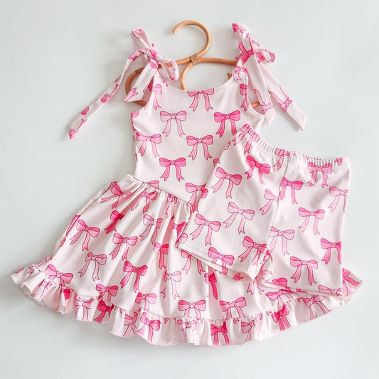 Pink activewear dress and biker shorts set with a playful bow print, ruffled hem, and shoulder ties.
