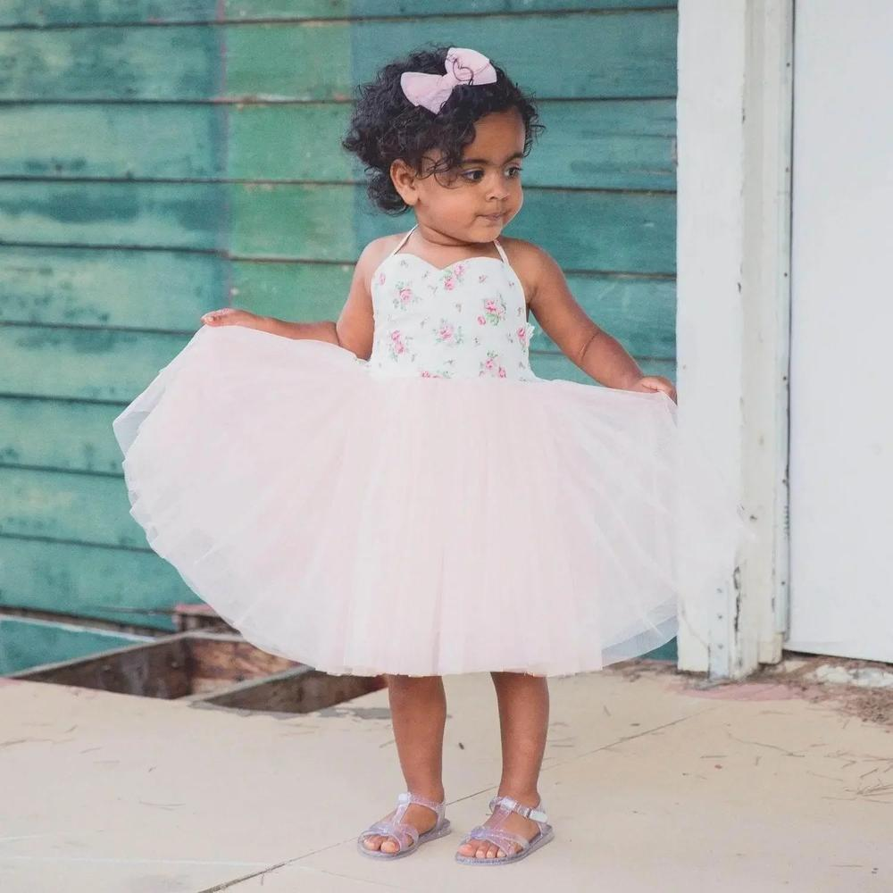 Toddler girl in pink tulle dress with floral bodice and bow headband, standing outside