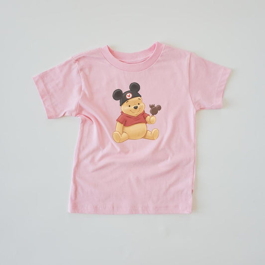 Pink Winnie the Pooh kids' t-shirt with Pooh wearing The ears and holding a chocolate treat.
