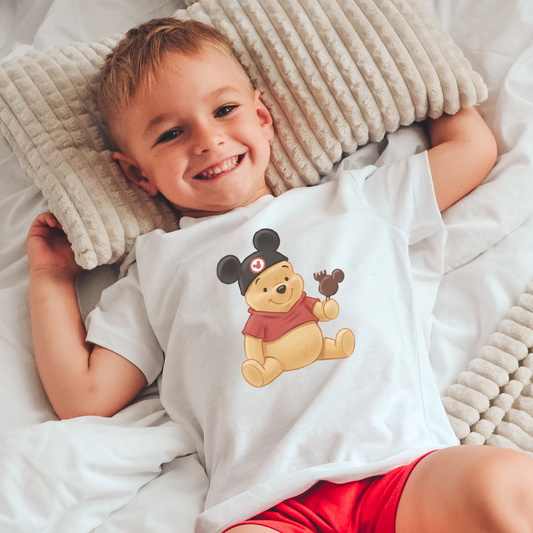 Child wearing a shirt with a cartoon character, lying on a bed with beige pillows.