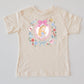 Beige Wonderland kids' t-shirt with Alice in a floral frame, pink bow, playing cards, and teacup design.