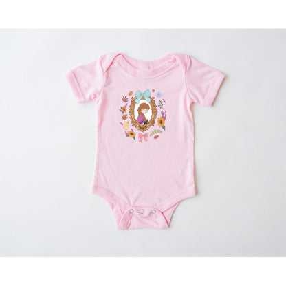 Pink infant onesie with a Wonderland character design in a gold frame surrounded by colorful flowers.