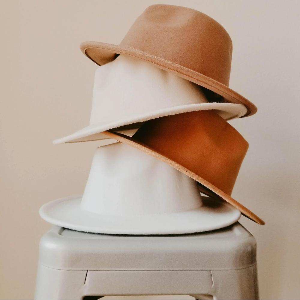 Stack of three classic brim hats in tan, cream, and brown on a stool, minimal background