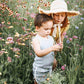 Young boy in light clothes and girl in straw hat exploring wildflowers in a sunlit meadow.