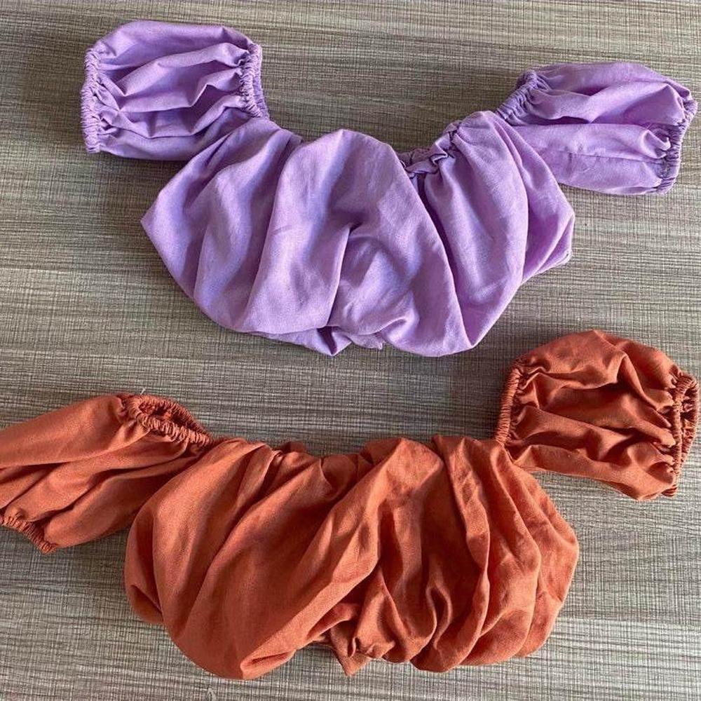 Two puff sleeve crop tops for children in lilac and rust colors on a textured surface