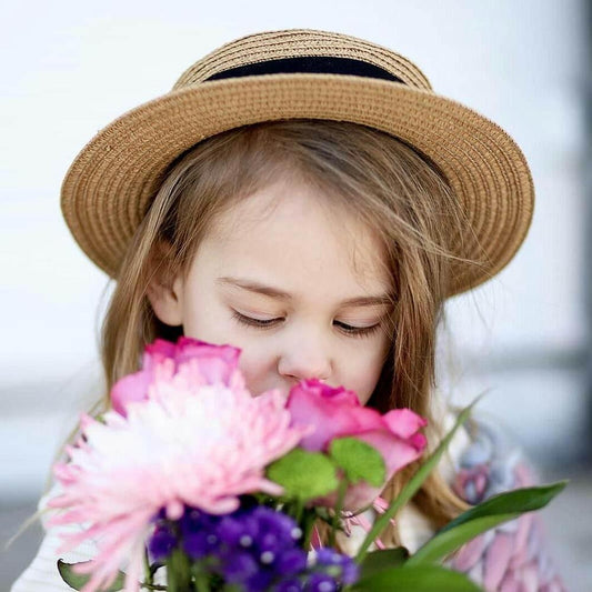Young girl in straw hat smelling colorful flowers, cute children's fashion close-up